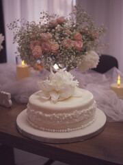 Elegant white celebration cake with delicate floral decoration, surrounded by soft tulle, candlelight, and fresh flower arrangements. Weding cake