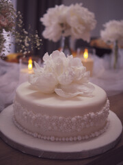 Elegant white celebration cake with delicate floral decoration, surrounded by soft tulle, candlelight, and fresh flower arrangements. Weding cake for bride