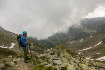 Adventure enthusiast hiking through dramatic rocky wilderness, using poles for stability while crossing steep terrain dotted with massive stones
