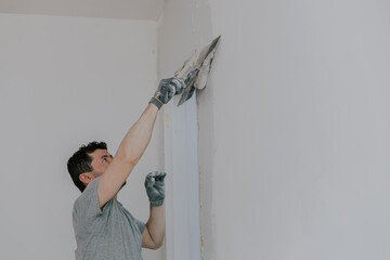 A young builder is plastering a wall near a doorway.