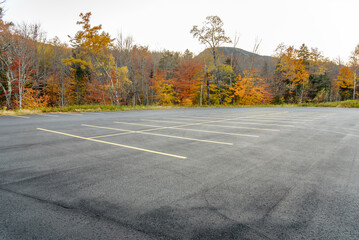 Empty car park surrouded by colourful autumnal trees in a mountain setting at dusk