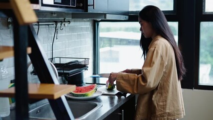 Woman cutting ripe and juicy watermelon on a white plate with a big knife cerac from a big window