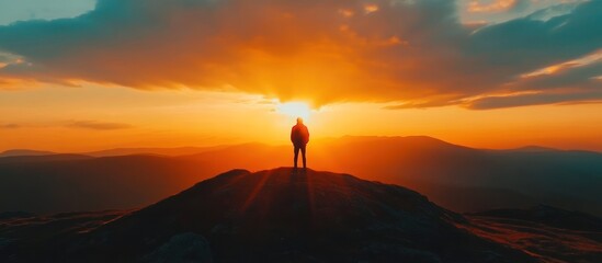 A lone person standing on top of a rocky mountain at sunset