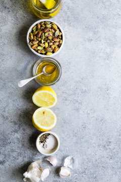 An overhead view of ingredients including pistachios, lemon halves, olive oil, garlic, and seasonings arranged neatly on a gray surface.