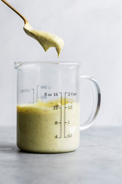A glass measuring cup filled with a creamy yellow sauce, with a spoon lifting some of it out.