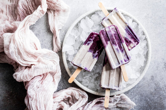 A plate of purple and white popsicles resting on ice, surrounded by a light pink fabric.