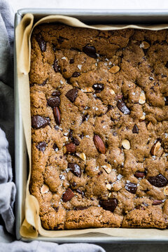 A freshly baked chocolate chip cookie bar with nuts and sea salt in a baking tray lined with parchment paper.