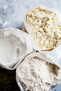 An overhead view of three bags containing different types of flour on a light surface.