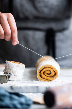 A person using string to cut a rolled cake on a floured surface.