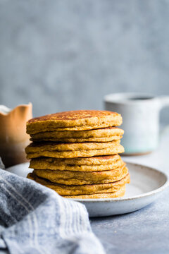 A stack of golden-brown pancakes on a ceramic plate with a blurred background of kitchen items.