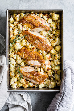 Oven-roasted chicken breasts with crispy cauliflower and herbs in a baking dish.