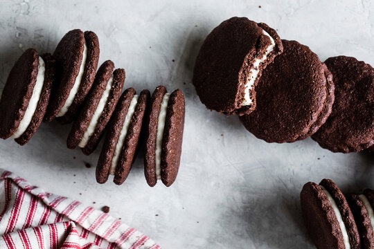 An assortment of chocolate sandwich cookies with white cream filling on a textured surface, alongside a red and white striped cloth.