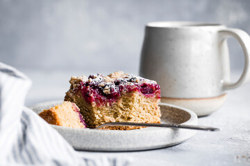 A piece of berry-topped cake on a plate with a mug in the background.