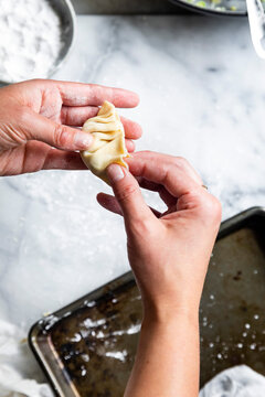 A person folds a dumpling on a floured surface.