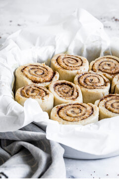 A batch of unbaked cinnamon rolls in a round baking dish lined with parchment paper.
