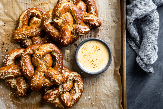 A tray of freshly baked pretzels with coarse salt served alongside a bowl of cheese dip.