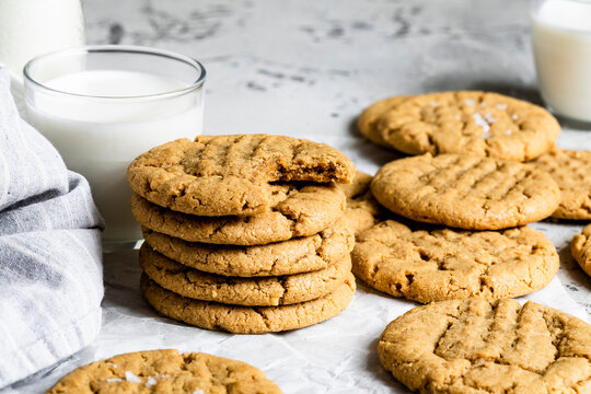 A stack of peanut butter cookies with a glass of milk on a light background.
