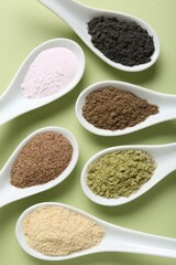 Different superfood powders in spoons on pale green background, flat lay