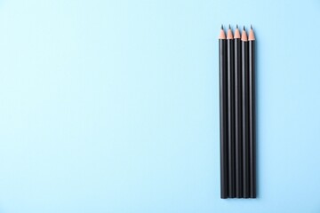 Many sharp graphite pencils on light blue background, flat lay. Space for text