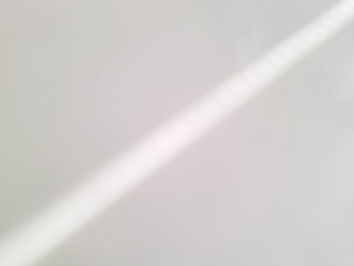 Diagonal beam of soft light casting subtle shadows on a plain white surface