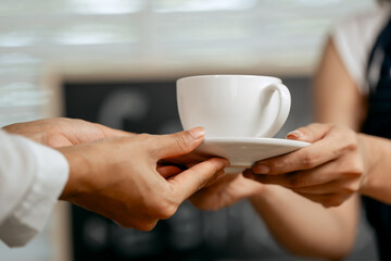 A young Asian female barista in a striped apron and orange shirt stands in a cozy modern café,...