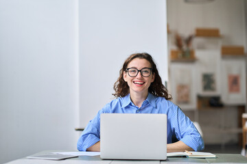 Portrait of young happy business woman company employee sitting at desk working on laptop. Smiling...
