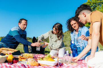 Happy family having fun, pouring water and eating together at a picnic in a park