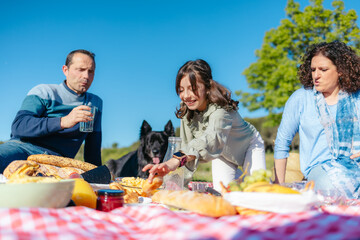 Happy family having fun, eating and playing with their dog during a picnic in nature