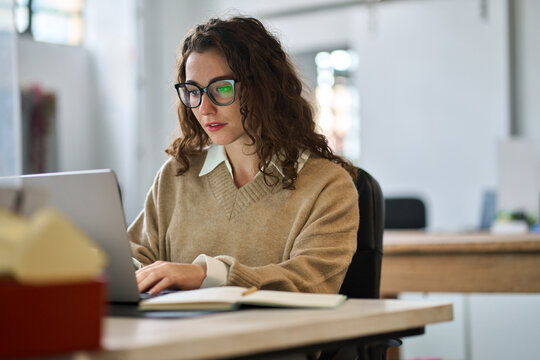 Smiling female student using computer technology learning online, doing web research. Young happy professional business woman worker employee sitting at desk working on laptop in corporate office.
