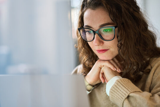 Fototapeta Busy professional business woman employee using laptop watching online webinar or training web course. Young serious student wearing glasses looking at computer, thinking, elearning, doing research.