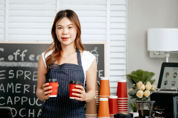 A young Asian female barista in a striped apron carefully pours steamed milk to create intricate...