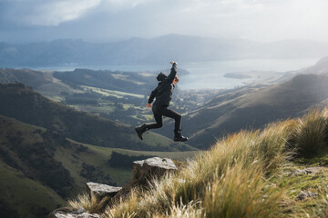 A man jumps on a rock on top of a mountain.