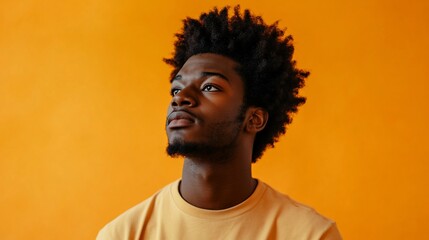 Portrait of a young man with afro hair against an orange background looking up