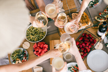 Group of friends toasting with wine over festive table with pasta, salmon, strawberries, watermelon