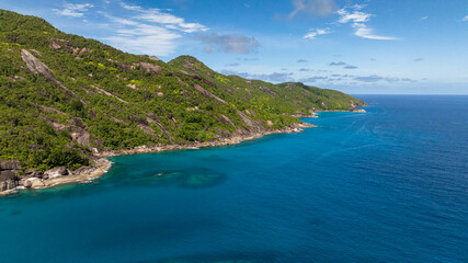 Green mountainous coastline descending into crystal clear turquoise waters under a blue sky....