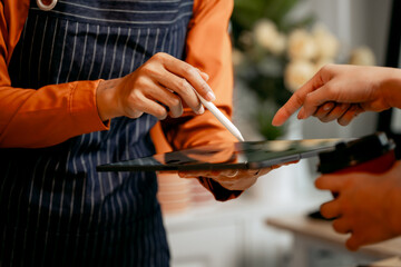 A young Asian female barista in modern cafe assists woman customer ordering latte, fresh coffee...
