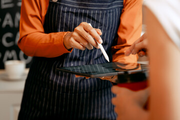 A young Asian female barista in modern cafe assists woman customer ordering latte, fresh coffee beans, dark roast, croissant, completing the purchase with mobile payment at the POS using QR code.