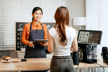 A young Asian female barista in modern cafe assists woman customer ordering latte, fresh coffee beans, dark roast, croissant, completing the purchase with mobile payment at the POS using QR code.
