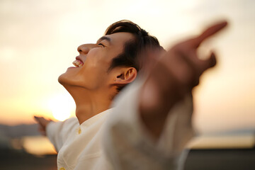 Joyful young man with outstretched arms embraces the warmth and freedom of the sunset.