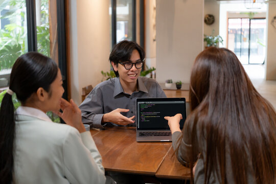 Programmer showing programming code on laptop screen to colleagues during informal team meeting, software engineer discussing project logic and development workflow with team members.
