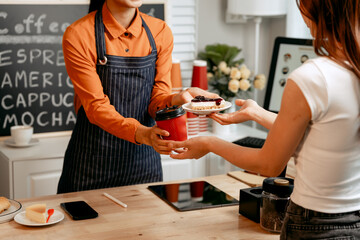 A young Asian female barista in modern cafe assists woman customer ordering latte, fresh coffee beans, dark roast, croissant, completing the purchase with mobile payment at the POS using QR code.