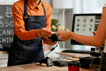 A young Asian female barista in modern cafe assists woman customer ordering latte, fresh coffee beans, dark roast, croissant, completing the purchase with mobile payment at the POS using QR code.