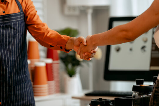 A young Asian female barista in modern cafe assists woman customer ordering latte, fresh coffee beans, dark roast, croissant, completing the purchase with mobile payment at the POS using QR code.