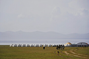 Yurts and riders on steppe by lake in Kyrgyzstan