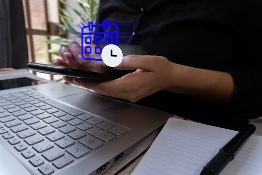 A businesswoman holds a cell phone with calendar and clock icons floating above it. In front is a laptop.