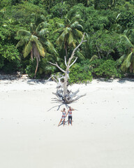 Aerial view of young couple standing on dream white sand beach on Seychelles. Woman and man are holding hands and looking far away. Jungle palm background on Therese Island. 