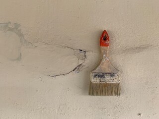 Paintbrush is leaning against a wall. The brush is old and worn, and the bristles are frayed. The wall is also old and has some damage, with a hole in it