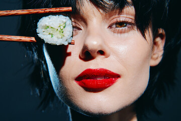 Stylish woman holding sushi with chopsticks, showcasing bold red lips and captivating gaze against...