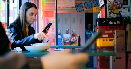 Businesswoman enjoys a tasty bowl of noodles while checking her smartphone in a vibrant chinese restaurant, blending modern technology with traditional cuisine