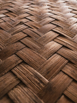 Close-up of traditional woven bamboo with a herringbone pattern. The texture highlights natural brown tones and craftsmanship in an organic, rustic material.